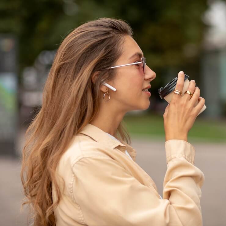 mujer bebiendo café con auriculares inalámbricos